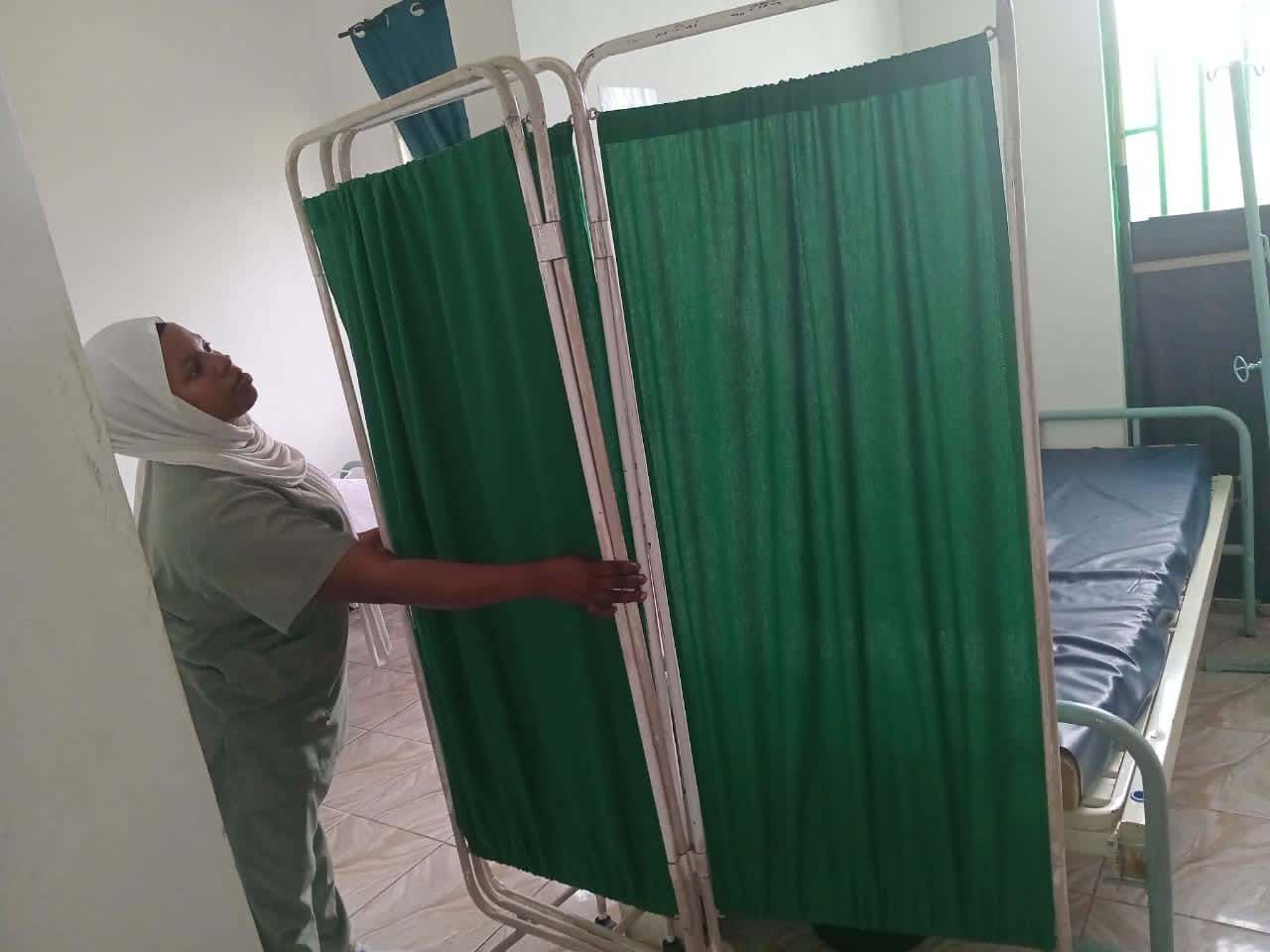 Nesi akiweka pazia la faragha kwa ajili ya mgonjwa.